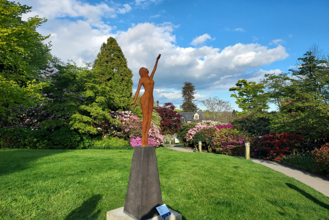 Statue of a woman pointing to the sky in the sunshine.